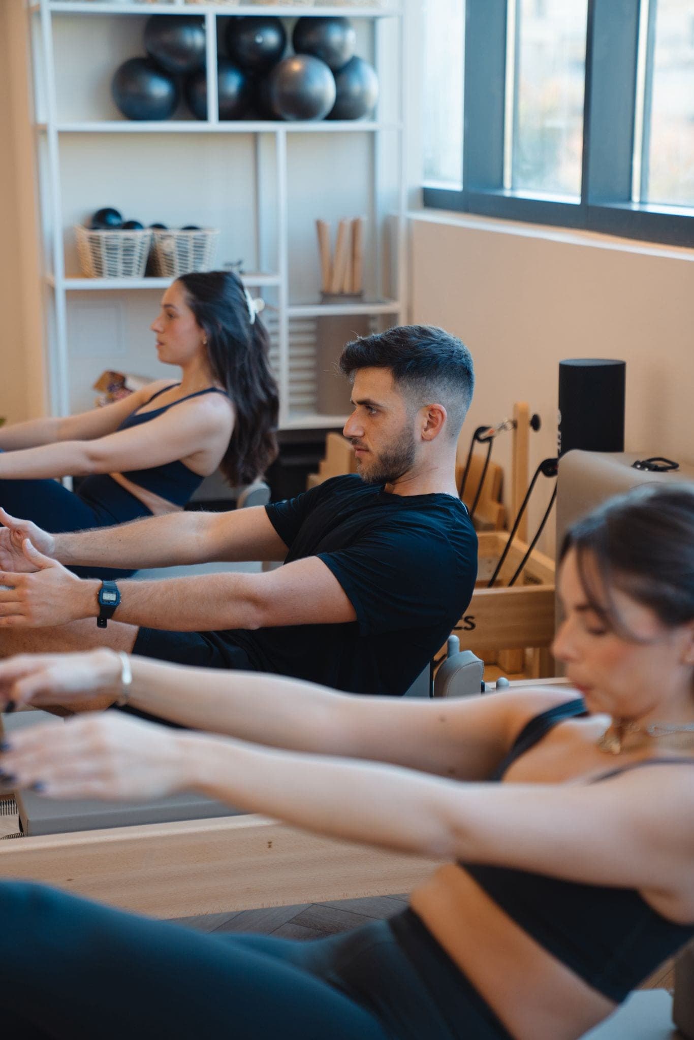 A student in a reformer Pilates class with arms extended at Studio M